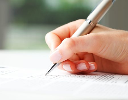 Businesswoman writing on a form Businesswoman's hand with pen completing personal information on a form